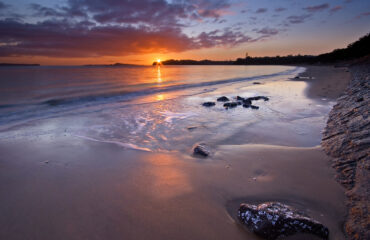 A sunset over the ocean with rocks in the water.