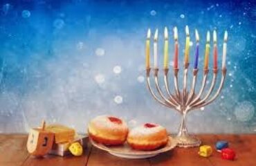 Menorah, donuts, and dreidels on wooden table.