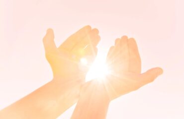 A person 's hands are stretched out in front of the sun.